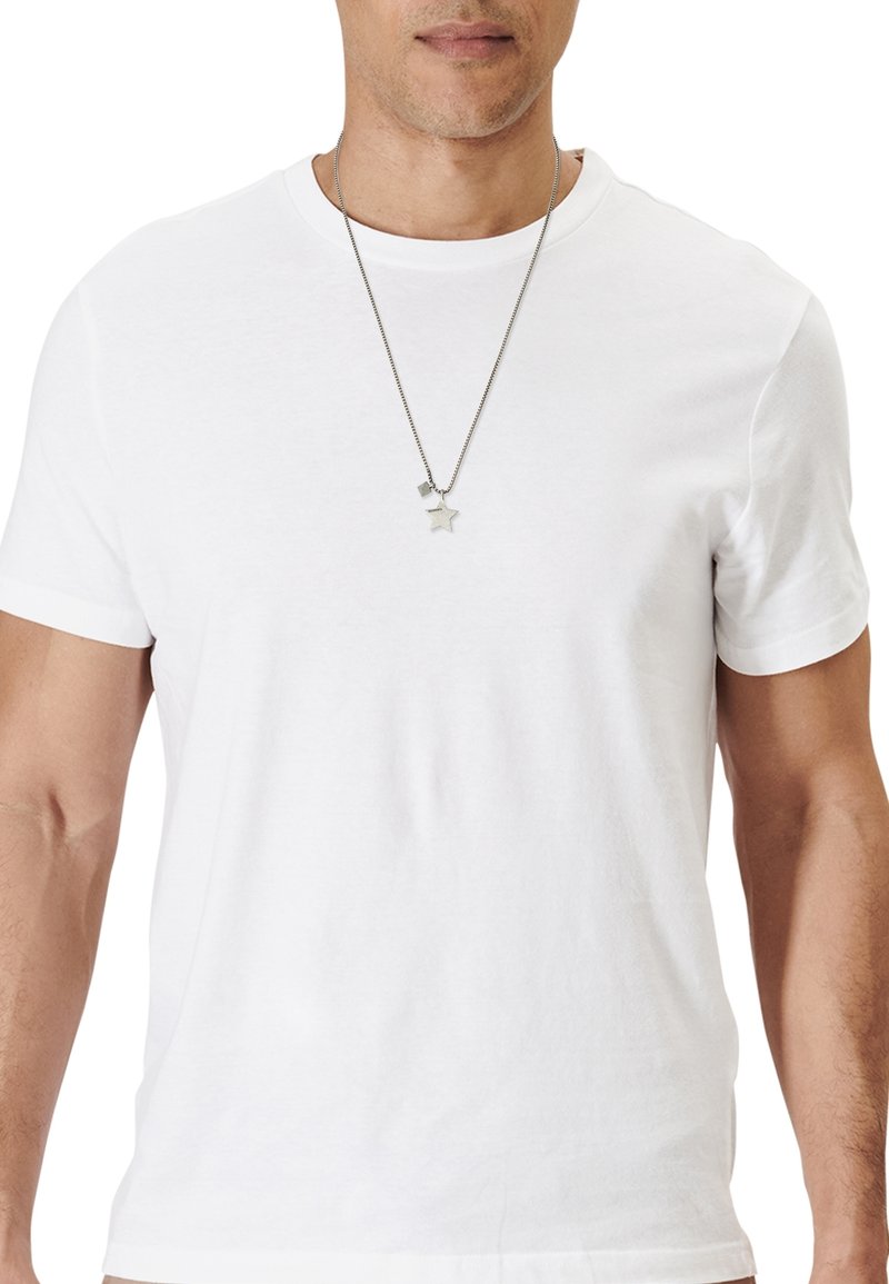 T-shirt en coton blanc avec un col rond et des manches courtes. Porté avec une longue chaîne argentée ornée d'un pendentif en forme d'étoile et de carré.