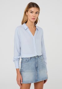 Camicia button-up azzurro chiaro con maniche lunghe, colletto e una texture liscia, abbinata a una mini gonna di denim blu sbiadito.