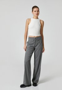 Wit geribbeld crop top gecombineerd met grijs gestreepte wijde broek. De broek heeft voorzakken en een knoopsluiting; het model draagt chunky zwarte schoenen.