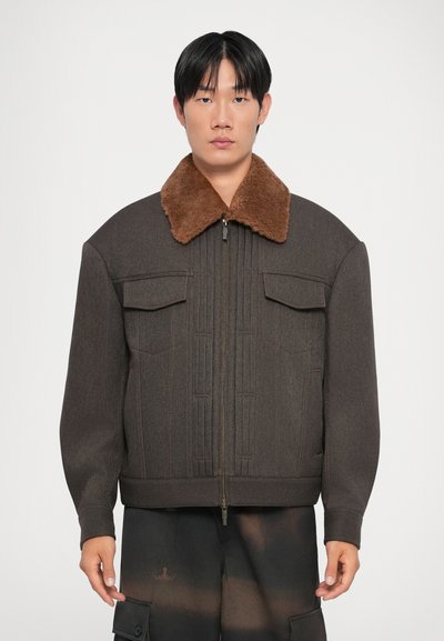 Veste en mélange de laine marron avec un col en fausse fourrure marron, des coutures verticales, deux poches poitrine et une fermeture à glissière à l'avant. Conçue avec une coupe décontractée.
