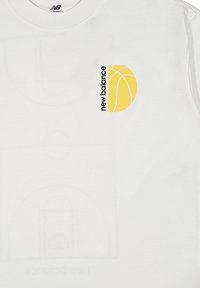 T-shirt bianca in cotone con una grafica di un pallone da basket giallo e il testo "new balance" in nero. Design semplice con una texture liscia.