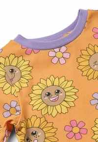 Orangefarbendes T-Shirt aus Stoff mit einem verspielten Muster von gelben Sonnenblumen mit lächelnden Gesichtern und rosa Blumen, ergänzt durch einen lavendelfarbenen Kragen.