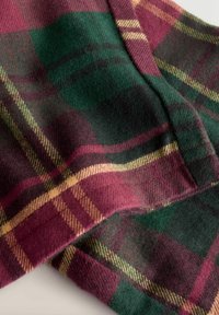 Wool blend fabric featuring a plaid pattern in deep red, green, and gold. Soft texture with diagonal stripes and woven detailing.
