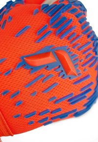 Rote Handschuhe mit strukturierten blauen Gummielementen, die ein meshartig gestricktes Design und dynamische Muster für verbesserten Griff und Flexibilität aufweisen.