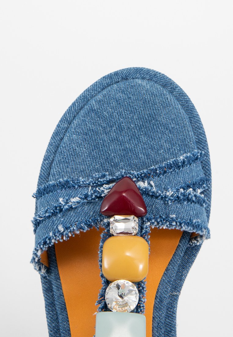 Sandalo in denim con bordi sfrangiati, dotato di una fascetta decorata con pietre colorate: rosse, gialle, trasparenti e turchesi.