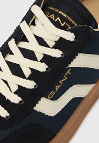 Temno modra superga z belimi vezalkami, belim valovitim trakom, gumijastim podplatom in zlatim napisom "GANT" na strani in jezikcu.