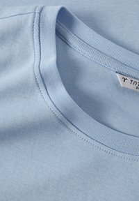 T-shirt en coton bleu clair avec un col rond, un col côtelé et une texture lisse, portant une petite étiquette sur la couture intérieure.