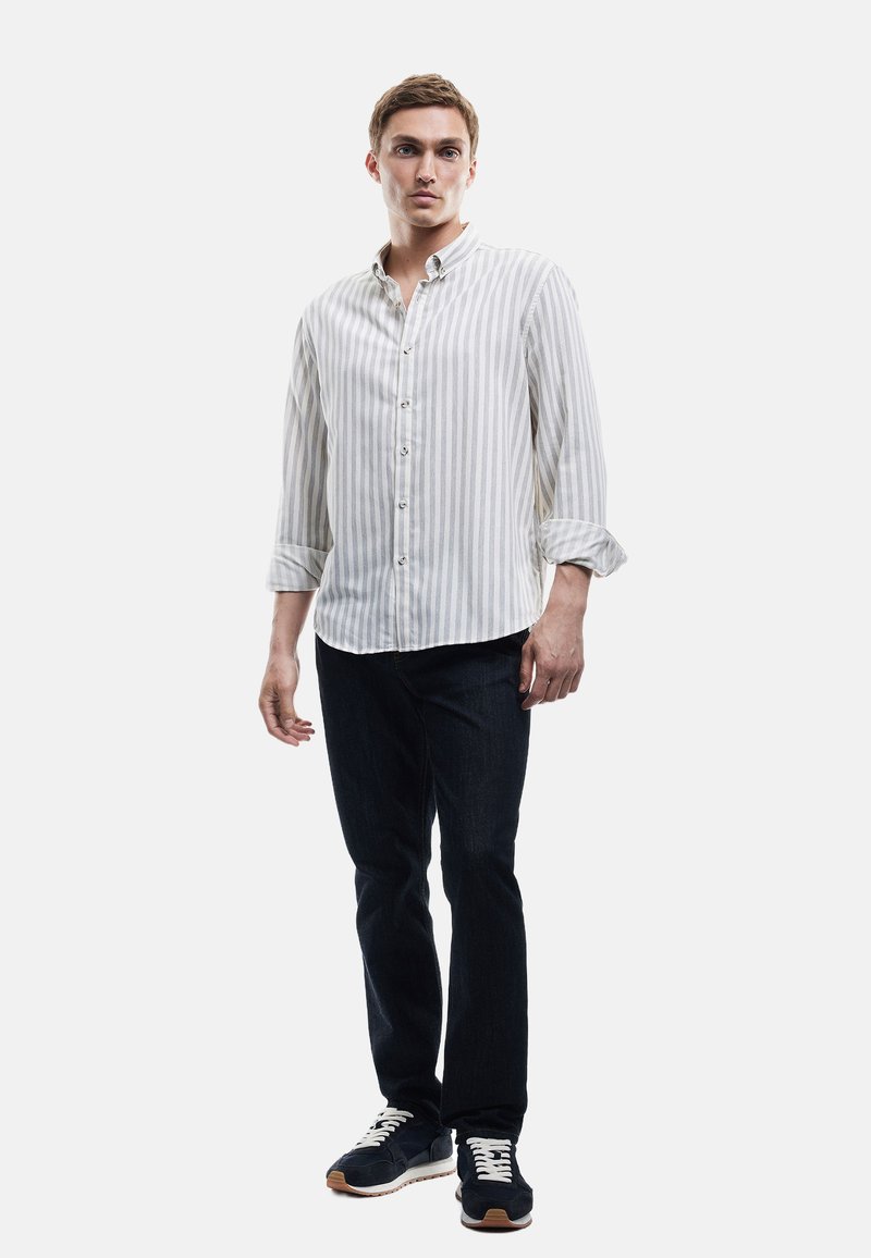 Stribet skjorte i lys beige og hvid, parret med mørke jeans og marineblå sneakers med hvide snørebånd og en gummisål.