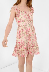 Květinové šaty z světlého růžového materiálu, s čtvercovým výstřihem, krátkými volánkovými rukávy a vrstevnatým lemem s drobnými květinovými vzory.