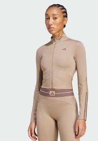 Completo sportivo in beige, composto da una maglia a maniche lunghe con zip e leggings aderenti. Texture a coste con sottili dettagli del logo in taupe.