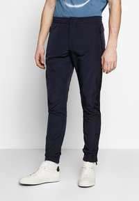 Marina joggers i lätt material med elastiskt midjeband, sidofickor med dragkedja och dragkedjor vid anklarna. Kombinerat med vita sneakers.