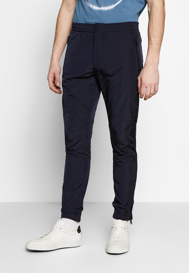 Marina joggers i lätt material med elastiskt midjeband, sidofickor med dragkedja och dragkedjor vid anklarna. Kombinerat med vita sneakers.