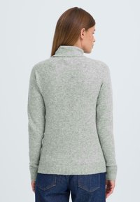 Hellgrauer, strukturierter Pullover mit hohem Kragen, gerippten Bündchen und Saum. Die Rückansicht zeigt eine figurbetonte Silhouette und minimalistische Details.