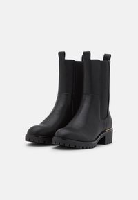 Botas de tobillo de cuero negro con paneles laterales de elastano, punta redondeada, suela de goma gruesa y un sutil acento dorado cerca del talón.