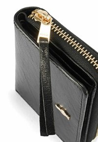 Czarny skórzany portfel z złotym zamkiem błyskawicznym i uchwytem, z małym złotym emblematem na przedniej kieszeni.