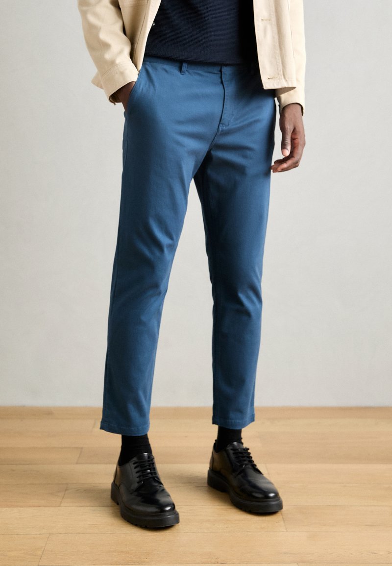 Kék pamut nadrág, slim fit szabással, oldalsó zsebekkel, sima textúrával és enyhe szűküléssel a bokán, feketére párosítva.