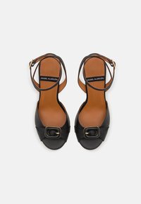 Black heeled sandals with a wide toe strap, square buckle detail, and tan insole; adjustable ankle strap with gold hardware accents.