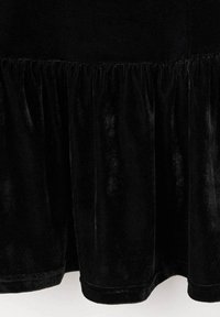 Czarna aksamitna spódnica z marszczonym szwem, tworzącym warstwowy, falbaniasty efekt w dolnej części.