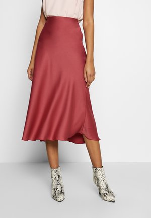 Femme portant une jupe midi en satin taille haute couleur rouille avec une légère évasement et des bottines imprimé serpent blanc cassé.