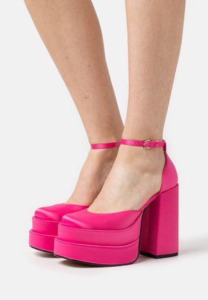 Talons compensés roses avec une finition lisse et brillante. Comprend un épais talon carré, un bout arrondi et une sangle ajustable à la cheville.