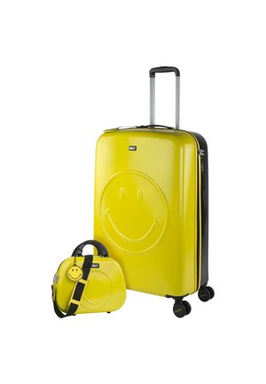 Maleta amarilla de concha dura y bolsa mini a juego, ambas con diseño de cara sonriente, acentos en negro, asa retráctil y ruedas para viajar.