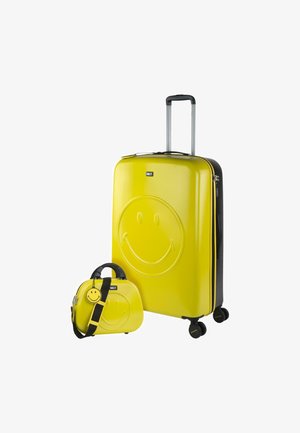 Maleta amarilla de concha dura y bolsa mini a juego, ambas con diseño de cara sonriente, acentos en negro, asa retráctil y ruedas para viajar.