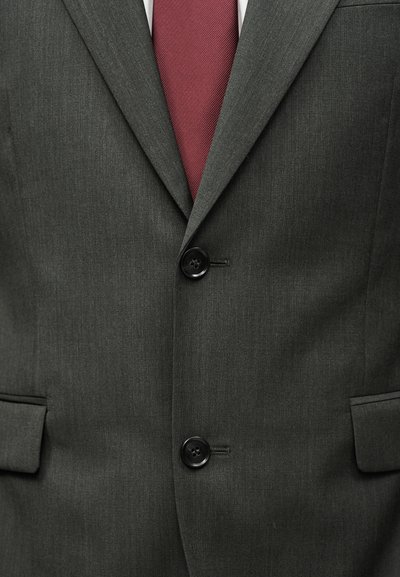 Σκούρο γκρι σακάκι με δύο κουμπιά κουμπωμένα, σε συνδυασμό με μπορντό γραβάτα πάνω από λευκό πουκάμισο.