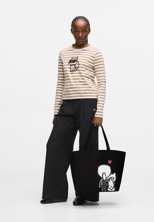 Gestreepte langjarige shirt in beige en wit met een kattenafbeelding. Zwarte rechte broek. Grote zwarte tote met een ontwerp van een witte figuur.