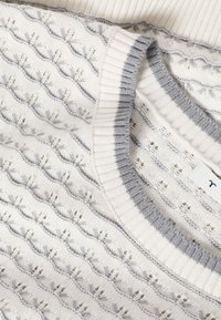 Λευκό πλεκτό πουλόβερ με γκρι σχέδια και ribbed γιακά, που δείχνει υφή ραφής και μια μικρή υφασμάτινη ετικέτα στο εσωτερικό του λαιμού.
