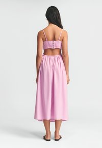 Rosa tvådelad outfit som består av en smockad croptopp med knappar på baksidan och en golvlång kjol med elastisk midja. Slät tygtextur.