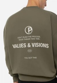 Sudadera verde oliva con cuello redondo y mangas largas. En la parte trasera tiene un texto en blanco que dice: "VALUES & VISIONS" con frases adicionales arriba y abajo.