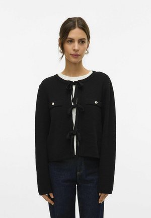 Cardigan court noir en tricot texturé, avec un col rond, deux poches avant et des fermetures à l'avant par lien.