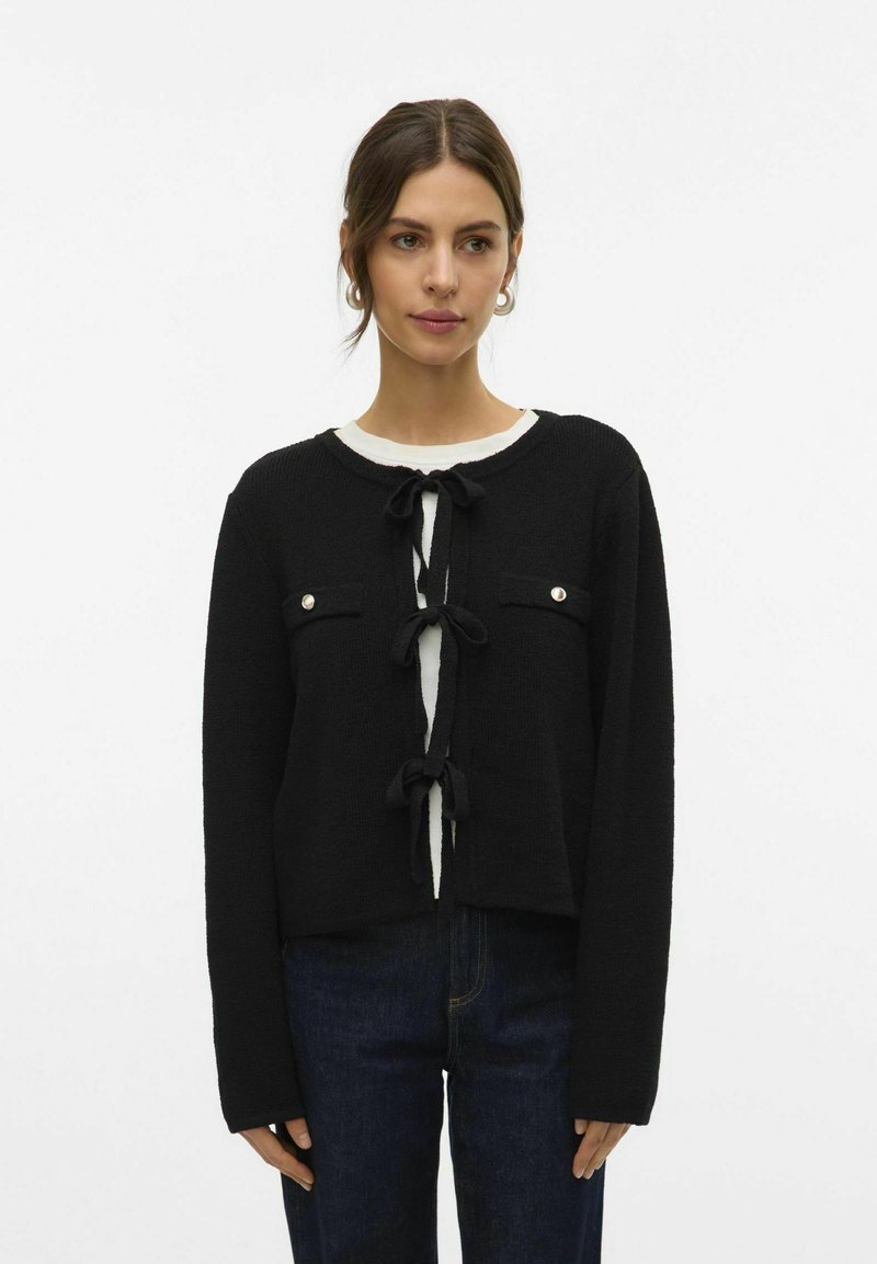 Cardigan court noir en tricot texturé, avec un col rond, deux poches avant et des fermetures à l'avant par lien.