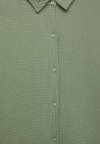 Chemise en tissu texturé vert clair avec un col et cinq petits boutons assortis alignés au centre devant.