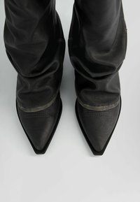 Stivaletti neri in pelle con punta affusolata, caratterizzati da un upper morbido e arricciato e un design minimalista. Accenti testurizzati lungo i bordi.