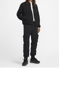 Černá bomber bunda se zipem a přední kapsou, doplněná o odpovídající cargo kalhoty a černé sportovní boty. Jednoduchý a funkční design.