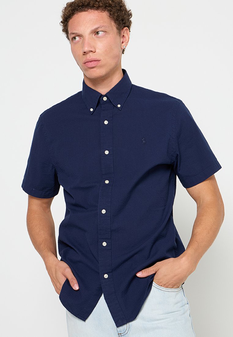 Chemise à manches courtes bleu marine avec un tissu texturé, dotée d'un col classique, de boutons sur le devant et d'un petit logo sur la poitrine.