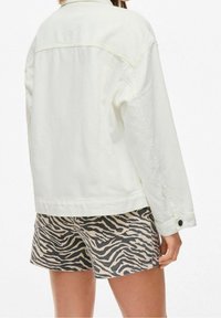 Vit denimjacka med avslappnad passform, med en ryggdetalj. Parat med mönstrade shorts i beige och svarta zebraränder.