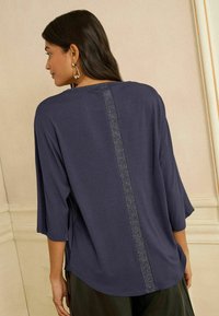 Tengerészkék felső laza szabással, háromnegyedes ujjal, hátul pedig texturált, csillogó függőleges csíkkal.