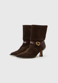 Brown suede ankle boots with pointed toes, a dark brown leather strap featuring a gold buckle, and a moderate heel.