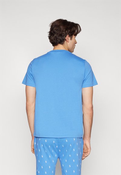 T-shirt azul de manga curta em tecido suave, com decote redondo e textura lisa. Usado com calças de pijama azuis estampadas.