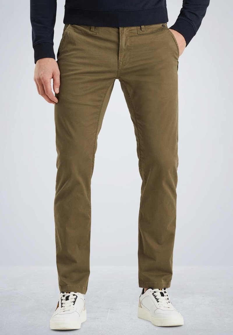 Kaki chinos lavet af bomuld, slim fit, med frontlommer, lynlås og båret med hvide sneakers. Glat tekstur og en ensartet farve.