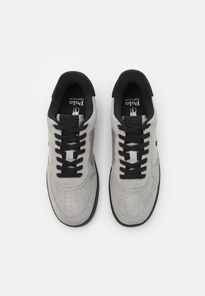Light gray sneakers with black accents, featuring suede and mesh material, perforated toe, and flat black laces. Logo on tongue.