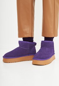 Bottines en suède violettes avec un bout rond, une semelle en caoutchouc contrastante et des coutures décoratives le long des coutures.