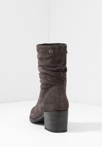 Bottine en suède gris avec un design plissé, bout rond et un talon en bois noir. Présente un petit accent en métal logo.