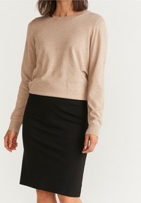Krémový svetr s dlouhým rukávem a kulatým výstřihem, doplněný černou úzkou tužkovou sukní. Měkčí textura, univerzální design.