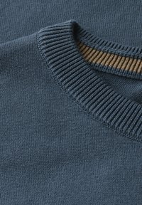 Blå stickad tröja med en ribbad halsringning och en kontrasterande beige rand. Mjuk textur, närbild som fokuserar på tyg och designdetaljer.