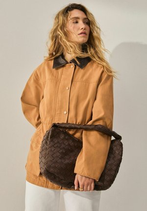 Braune Canvasjacke mit schwarzem Lederkragen, mit einer lockeren Passform. Gewebte braune Handtasche mit gepolstertem Tragegurt, in einer neutralen Umgebung präsentiert.