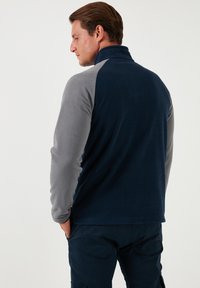 Fleece jacket with a high collar, featuring navy blue body and gray sleeves. Soft texture and a relaxed fit. Visible stitching detail.