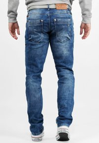Jeans en denim bleu clair avec un délavage, présentant des poches arrière et des accents cousus. Associés à des baskets blanches.